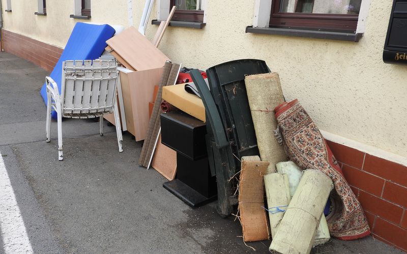Old chairs, rugs and a mattress piled against a wall, ready for a junk pickup photo